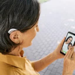 Senior woman with a hearing aid behind the ear communicates with her daughter and granddaughter via video communication via a smartphone. Full human life with hearing aids