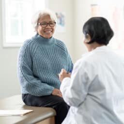 Older female patient sitting on exam table talking with her doctor.