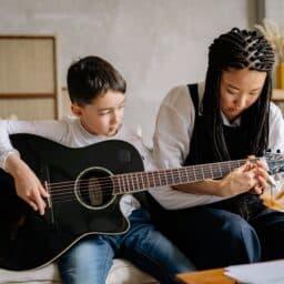 Woman teaches a young boy how to play guitar.