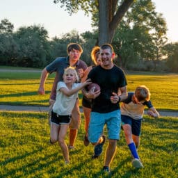 Young Family of five enjoying touch football together in the early evening at a park