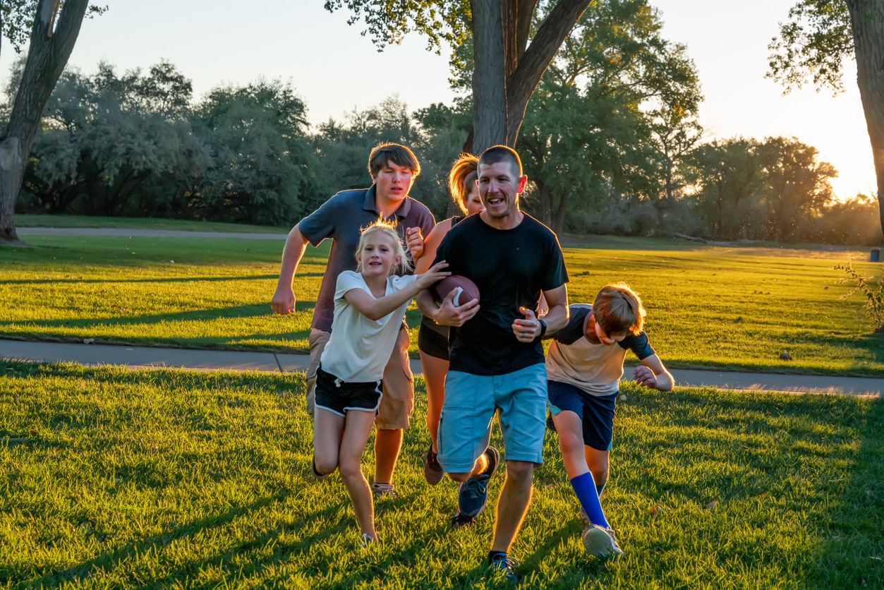 Young Family of five enjoying touch football together in the early evening at a park