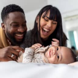 Two happy parents playing with their smiling baby.
