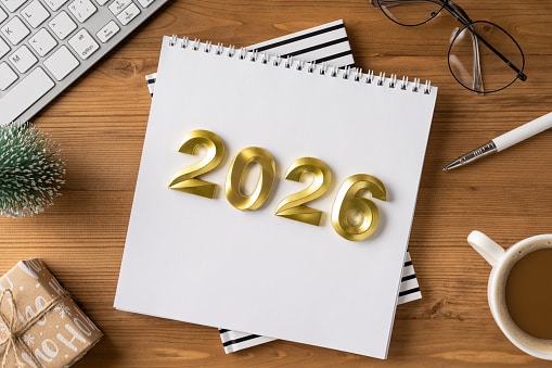 A desk scene for year end and holiday plans with a 2026 calendar, gift, coffee, and office items suggesting Christmas and New Year greetings